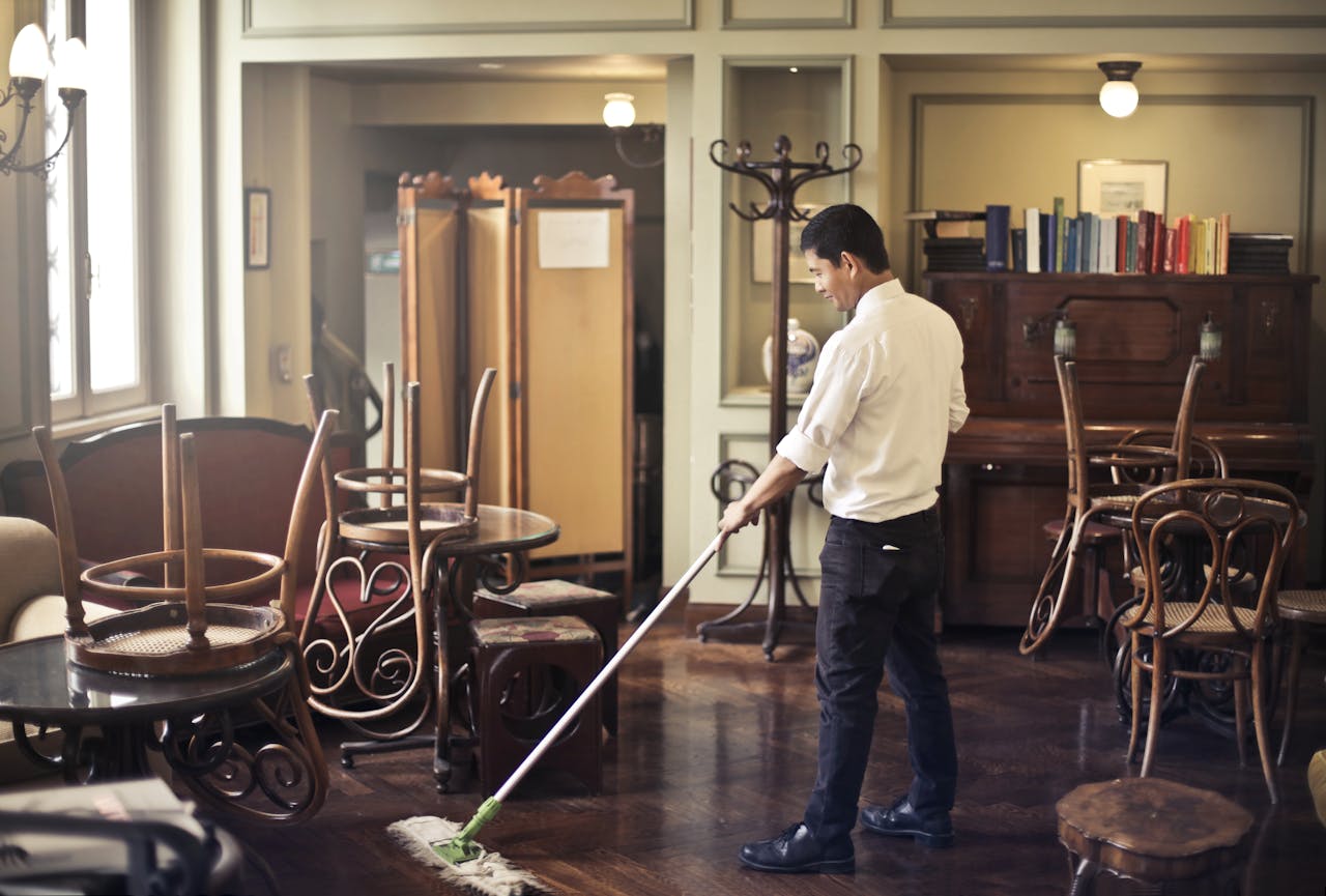 team-04 Side view of young ethnic male in uniform cleaning floor with mop while working in retro styled restaurant