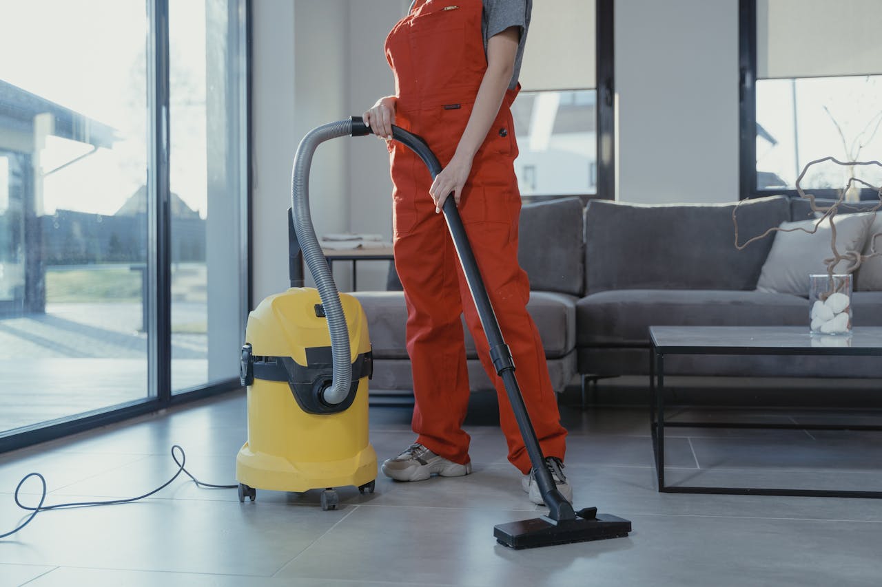 team-03 A professional cleaner in red coveralls vacuuming a modern living room with a yellow vacuum cleaner.